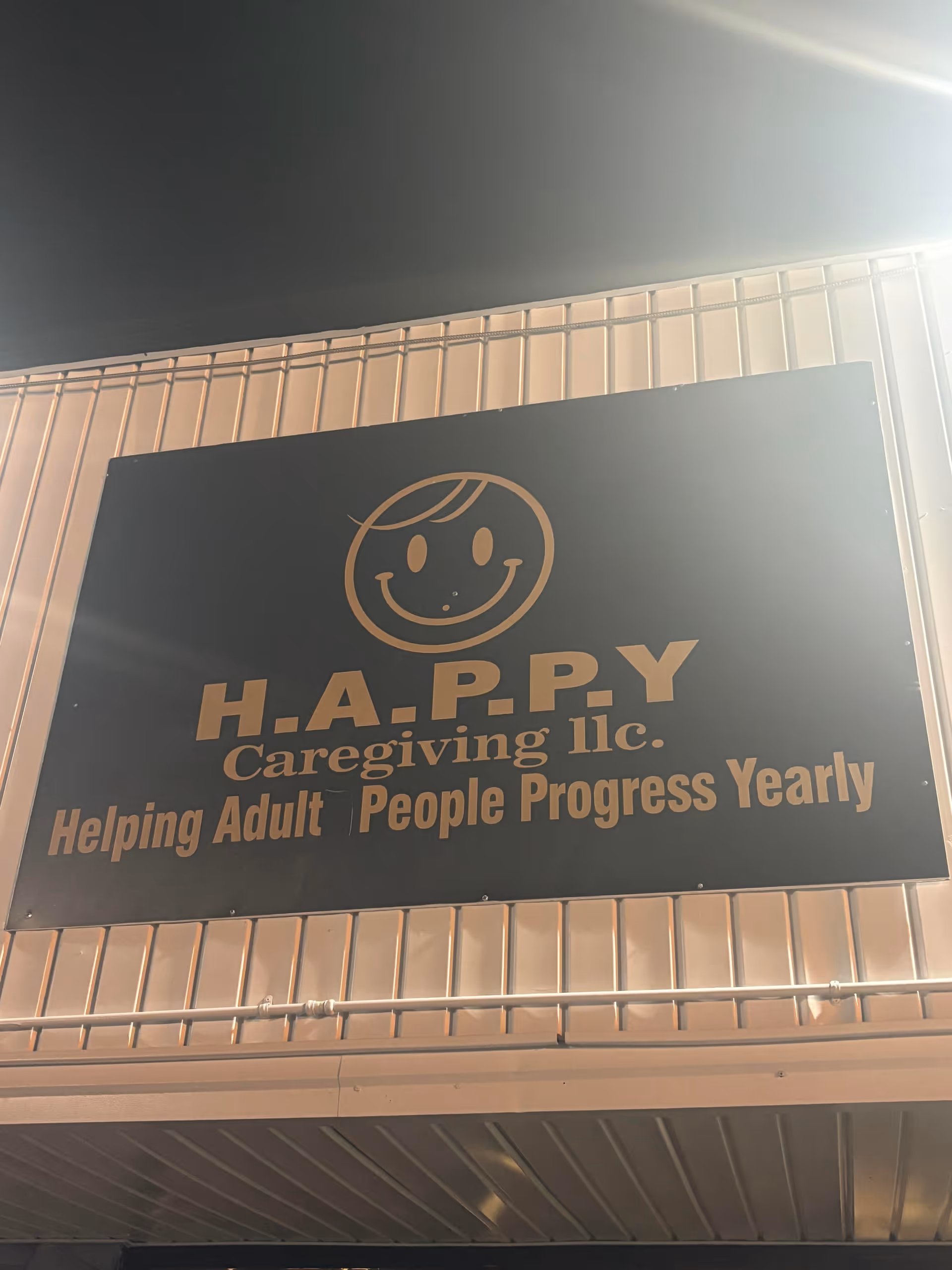 Sign displaying H.A.P.P.Y Caregiving LLC and a smiley logo on the wall.