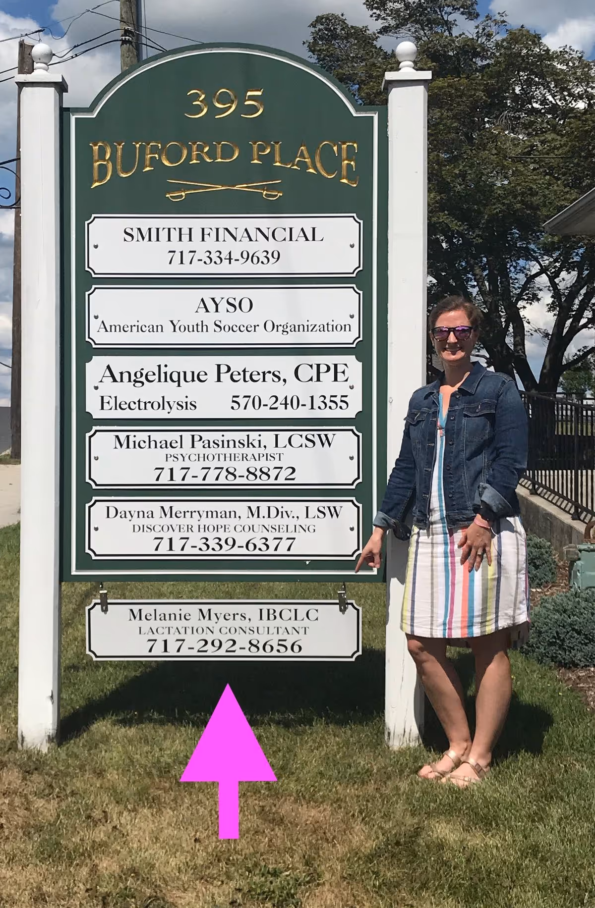 Woman stands beside a tall green directory sign outside a building.