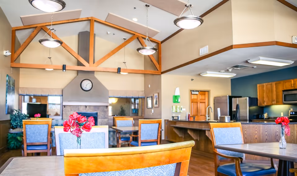 Spacious senior living dining area with tables, chairs, and a kitchen counter.