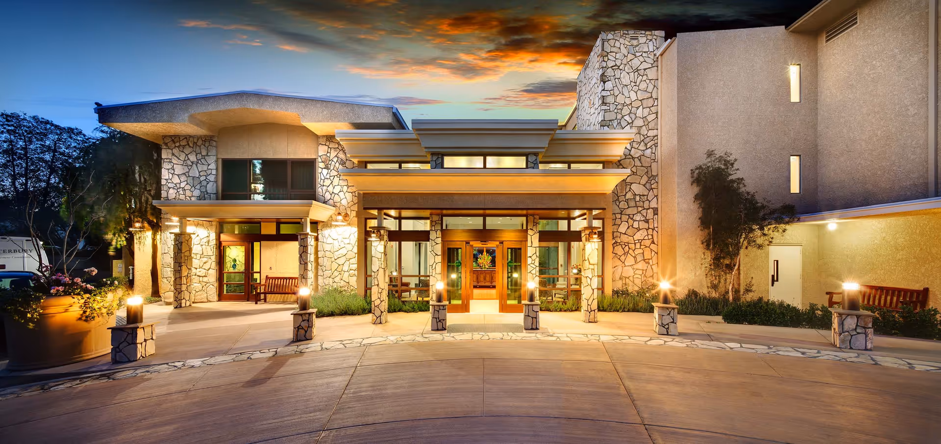 Front entrance of a stone-faced senior living community building lit at dusk.
