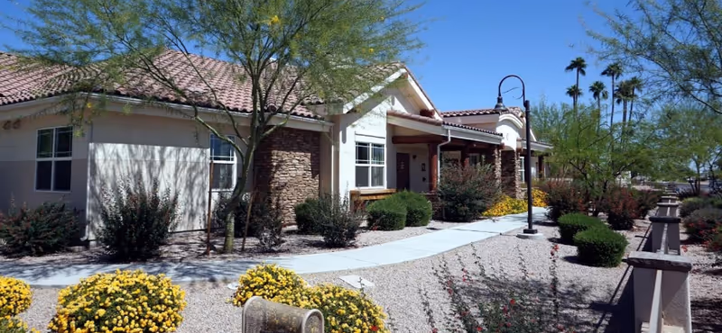 Sun City West memory care exterior with a curved walkway, desert landscaping, and a single-story building.