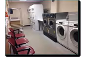 Laundromat-style facility with front-loading washers, dryers, and pink chairs along the wall.