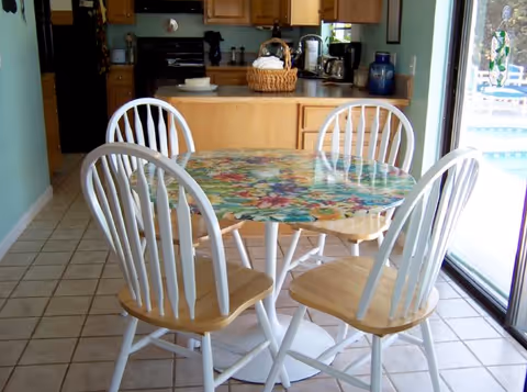 Bright dining area at East Side Home with floral tablecloth and white wooden chairs.