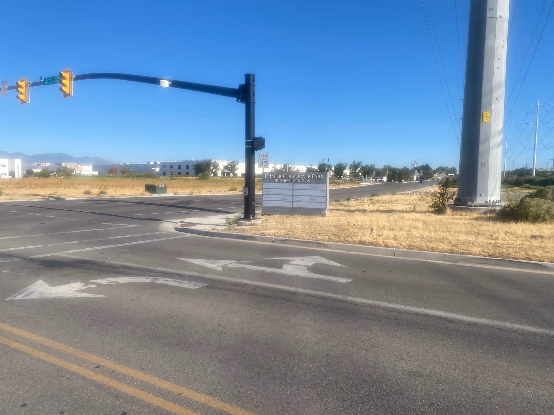 Wide intersection with traffic light, utility pole, and a sign near a vacant lot.