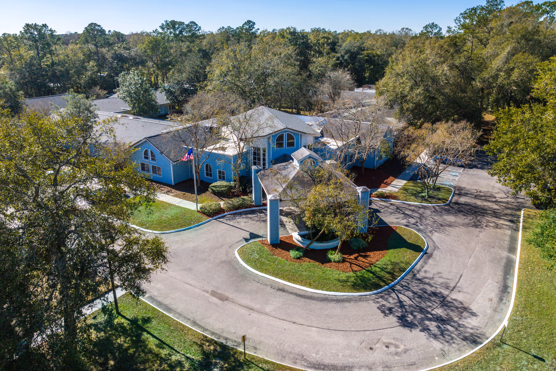 Aerial view of a blue senior living center with a circular driveway and surrounding trees