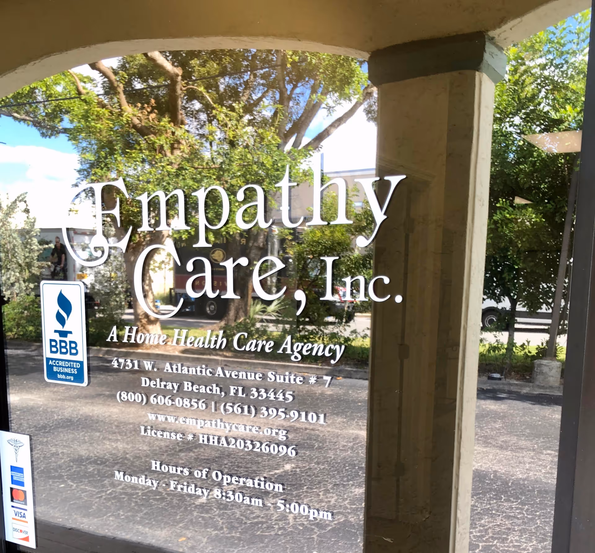 Glass door sign reading Empathy Care, Inc. with details, reflecting trees outside