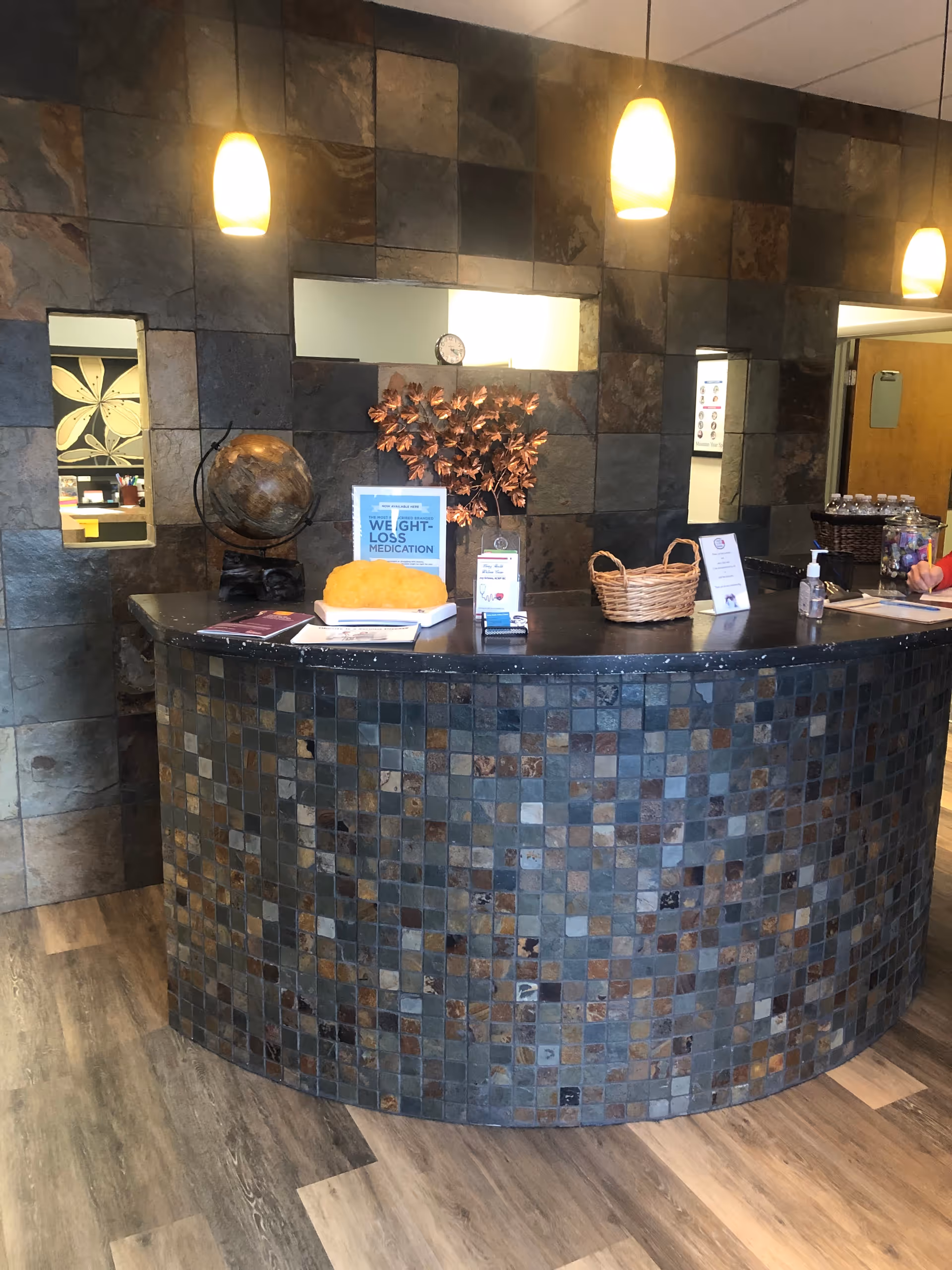 Curved mosaic-tiled reception desk in a tile-walled interior lobby with pendant lights.