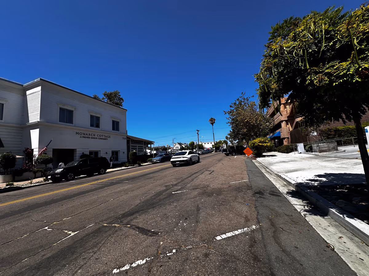 Street view showing the Monarch Cottage building on the left, a roadway with parked cars, and trees under a clear blue sky.
