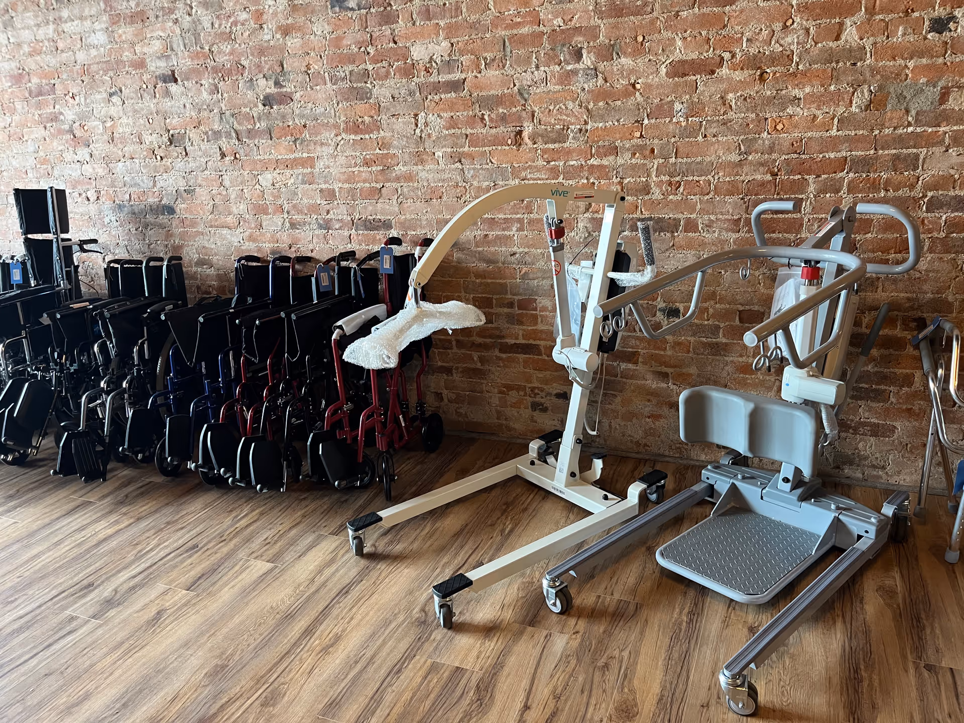 Wheelchairs and rehabilitation equipment arranged in a brick-walled interior room.