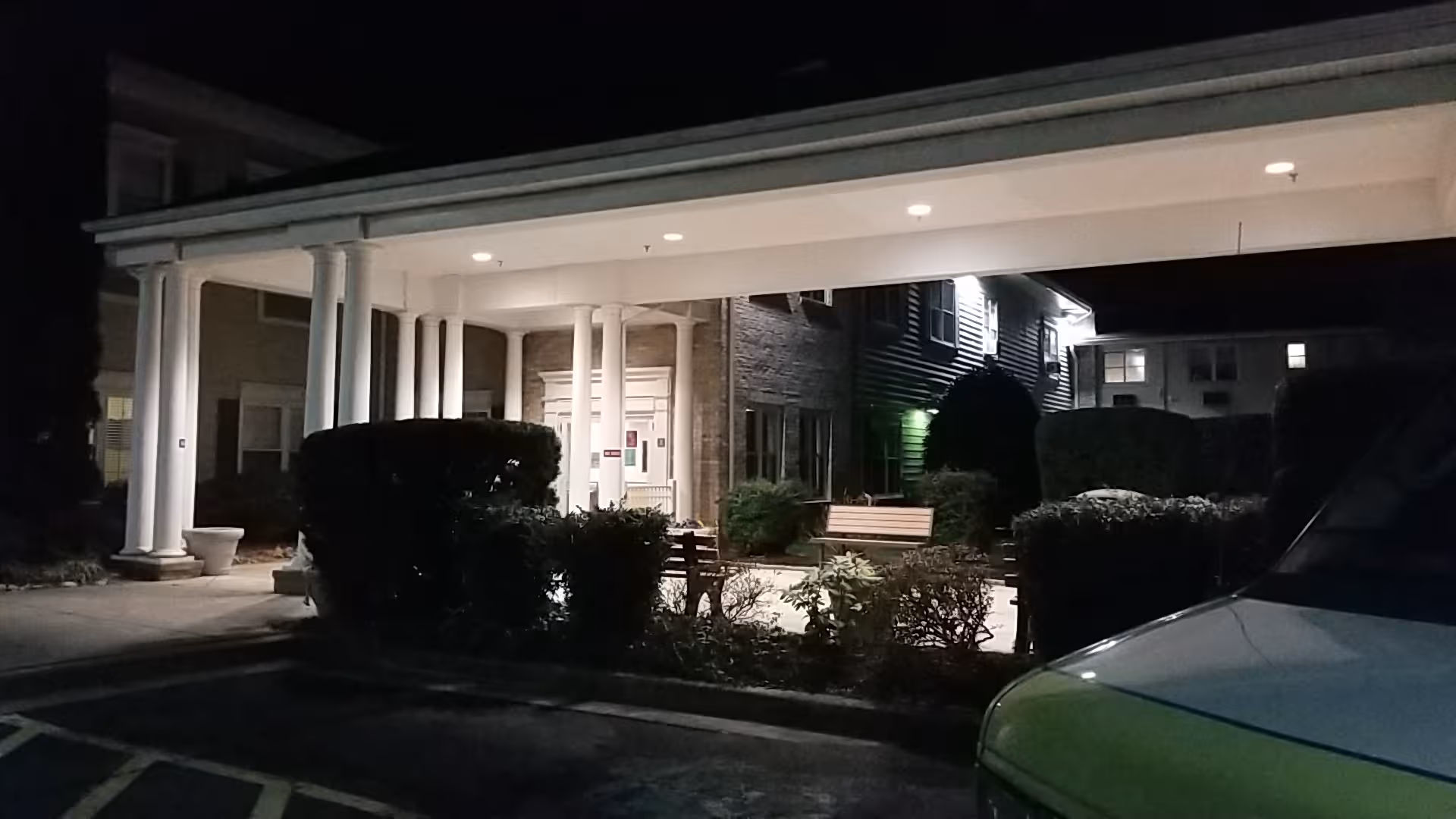 Night view of a senior living facility entrance with white columns and benches.