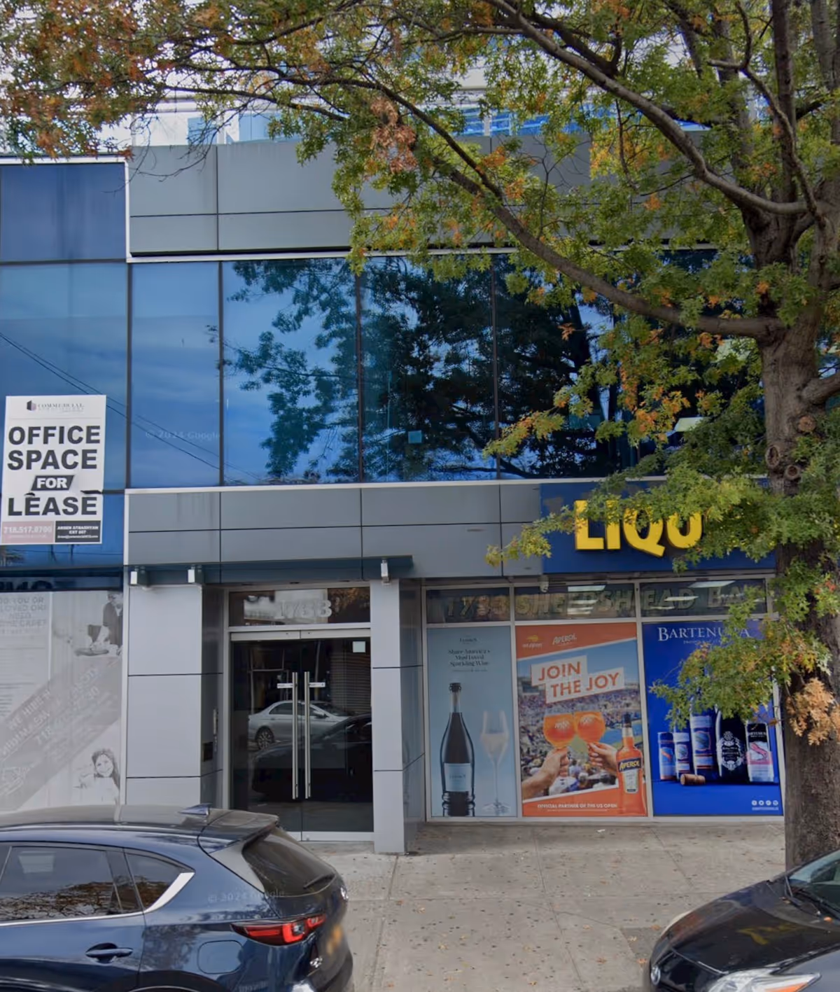 Modern glass-front building with large windows, a partial LIQU sign, and parked cars.