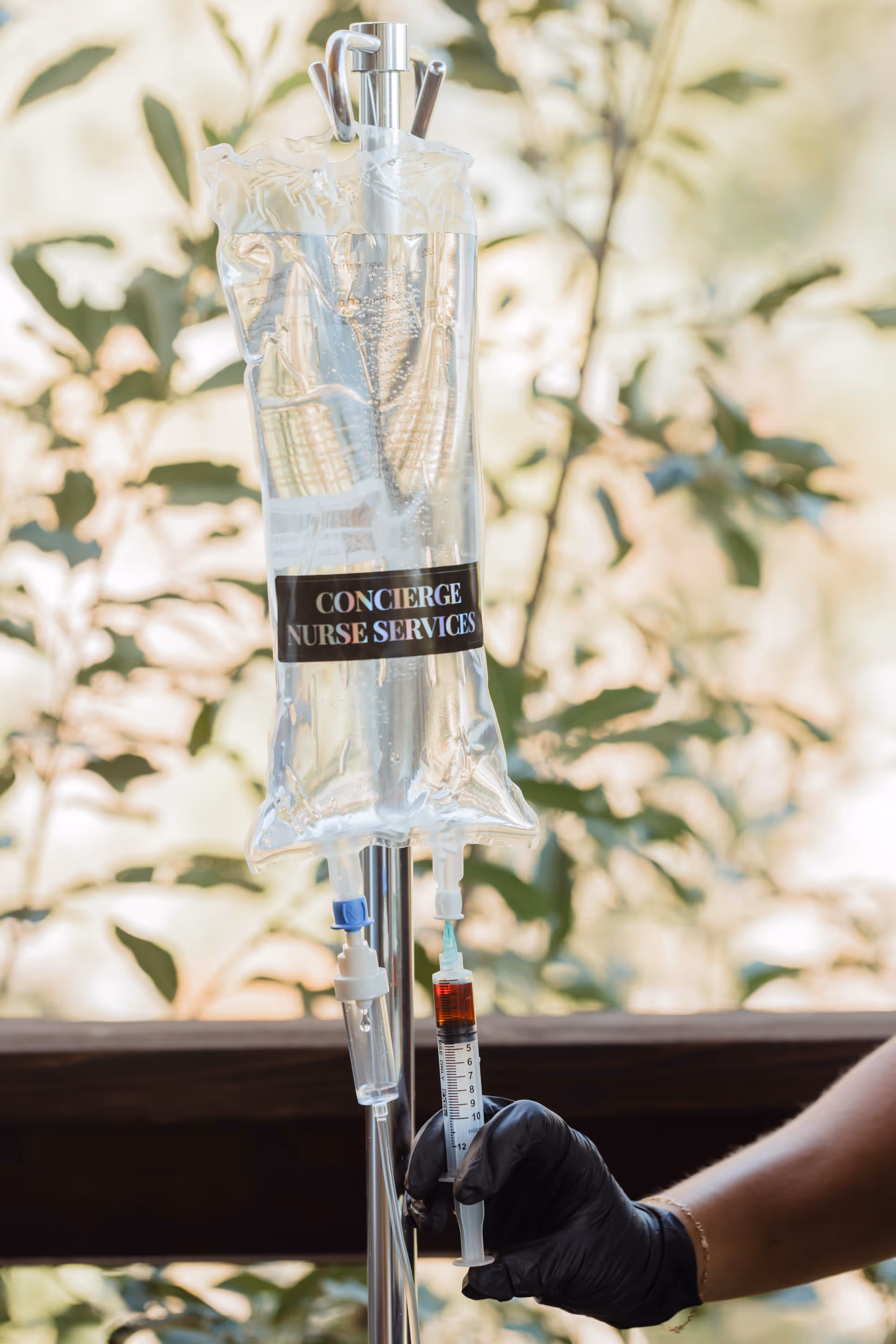 Intravenous drip bag labeled Concierge Nurse Services on a metal stand held by a gloved hand