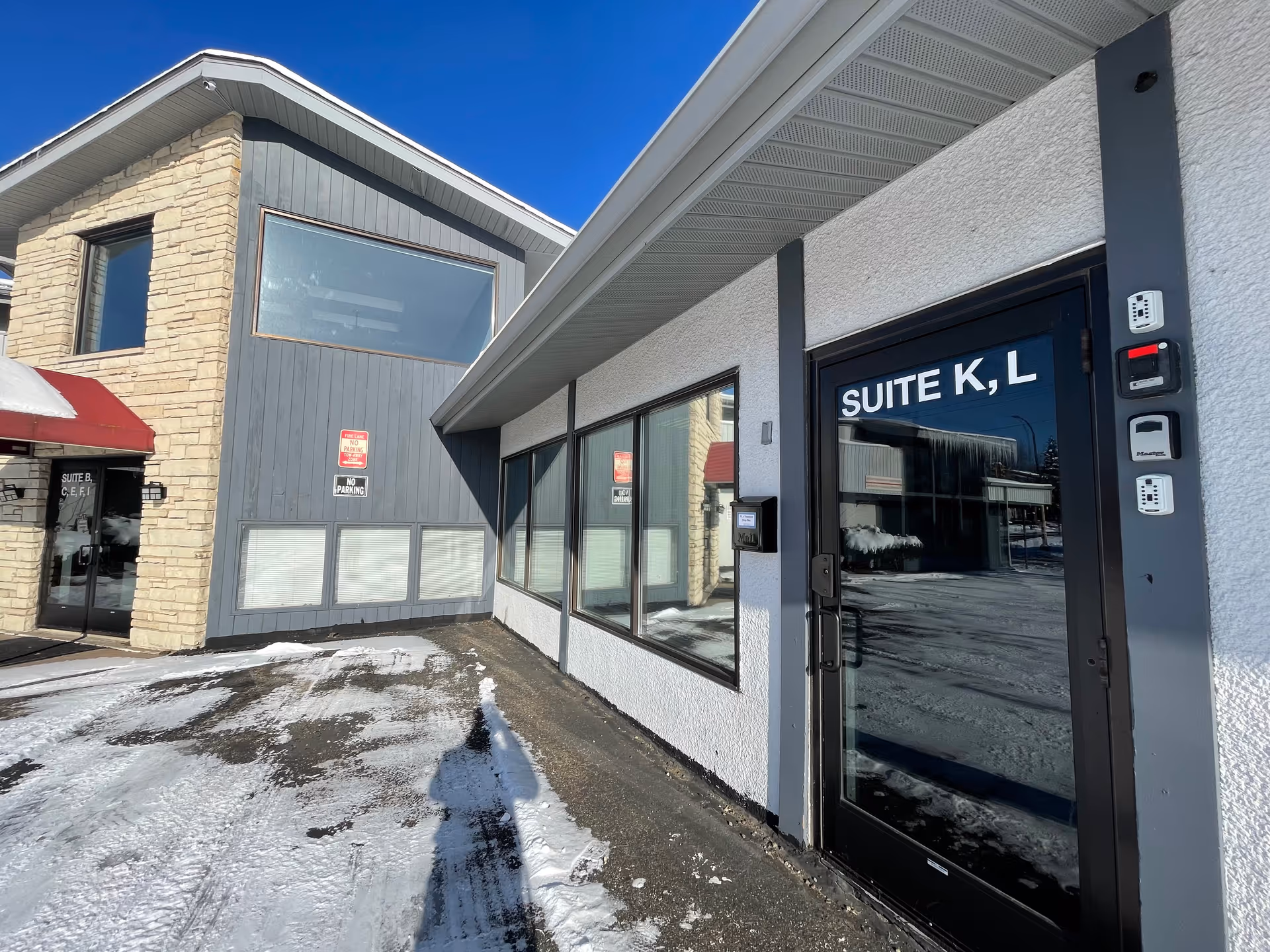 Exterior view of a front entrance with Suite K,L doors and snowy pavement.