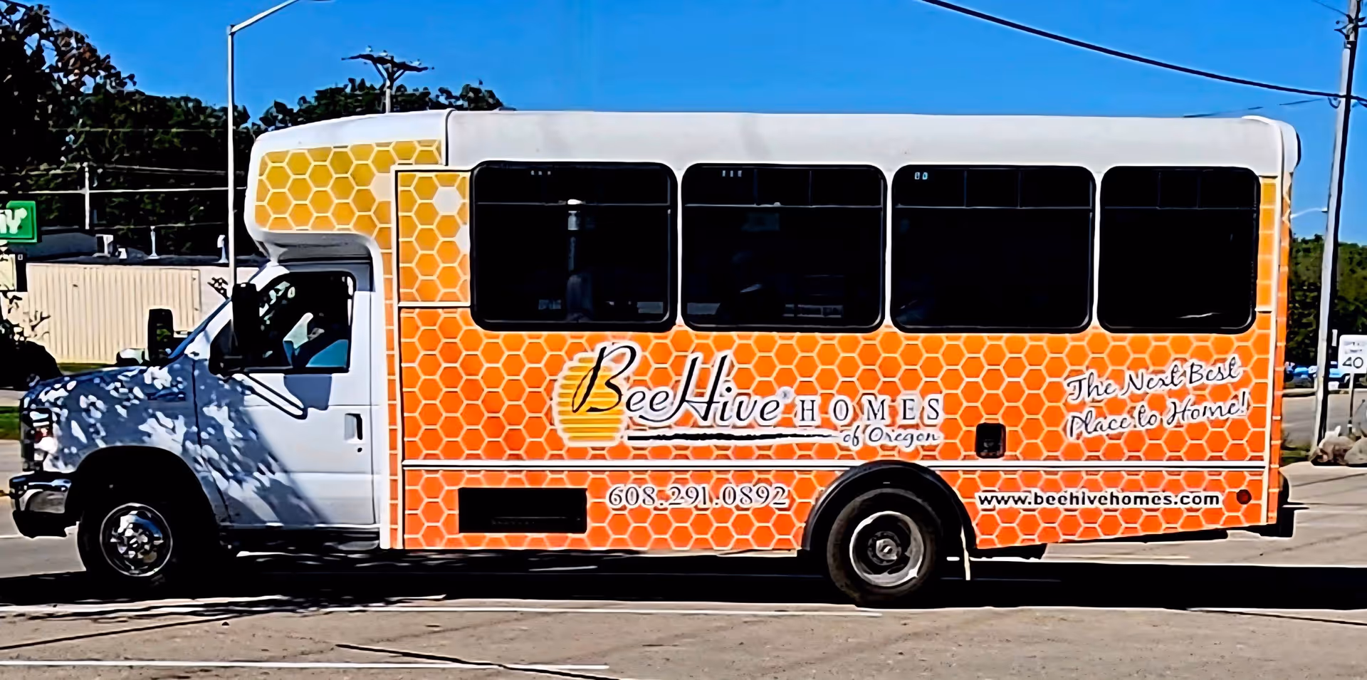 Orange honeycomb-patterned BeeHive Homes bus parked on a sunny street