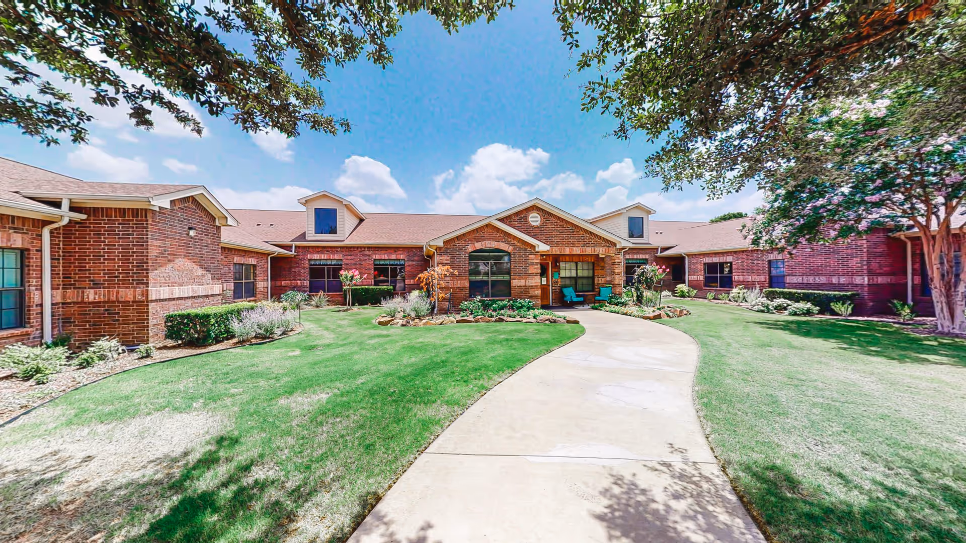 Exterior of Reliable Personal Care Home, brick building, curved walkway, green lawn, trees around entrance.
