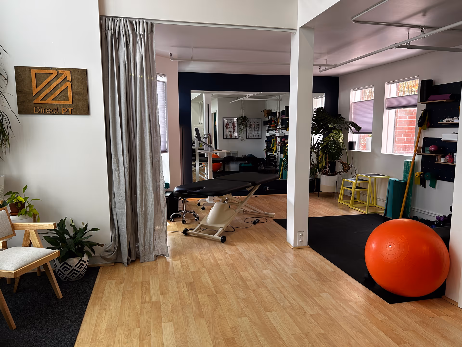 Indoor physical therapy room with a treatment table, equipment, and an orange ball.