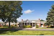 Front exterior of a single-story brick senior living facility with trees and a lawn.