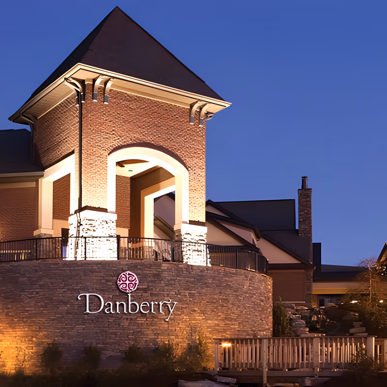 Exterior view of Danberry at Inverness building at dusk, featuring a well-lit brick and stone facade with an arched architectural design and a sign displaying the name 'Danberry'.