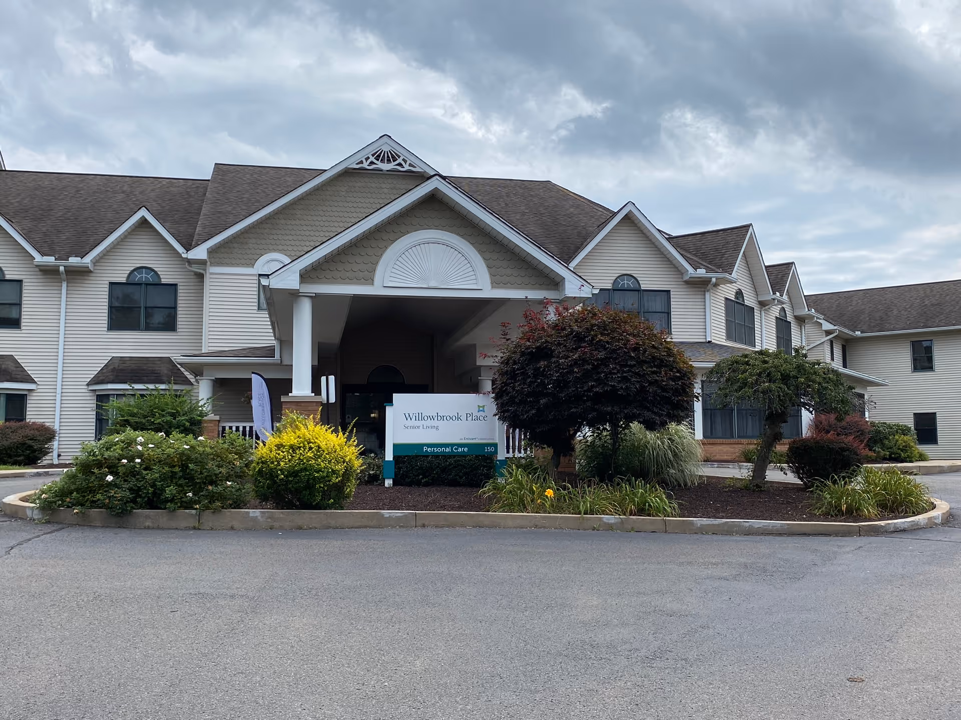 Exterior view of Willowbrook Place senior living facility with landscaped entrance and sign.