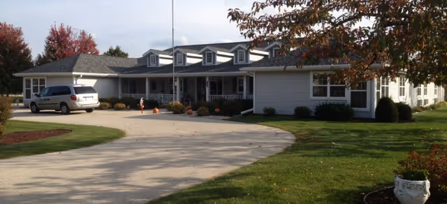Senior living facility with a curved driveway, manicured lawn, and a front entrance.