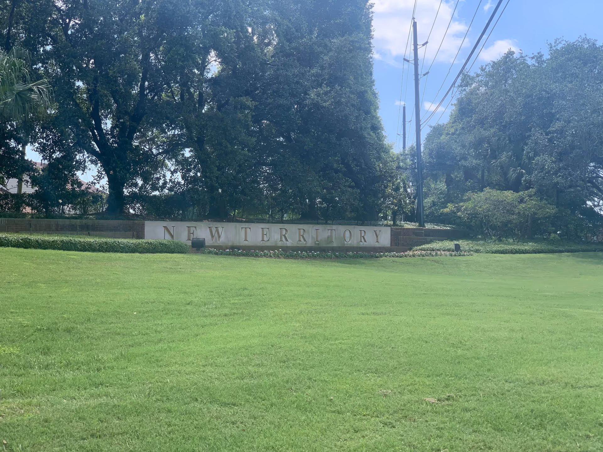 Well-manicured lawn with a low stone sign reading New Territory and tall trees.