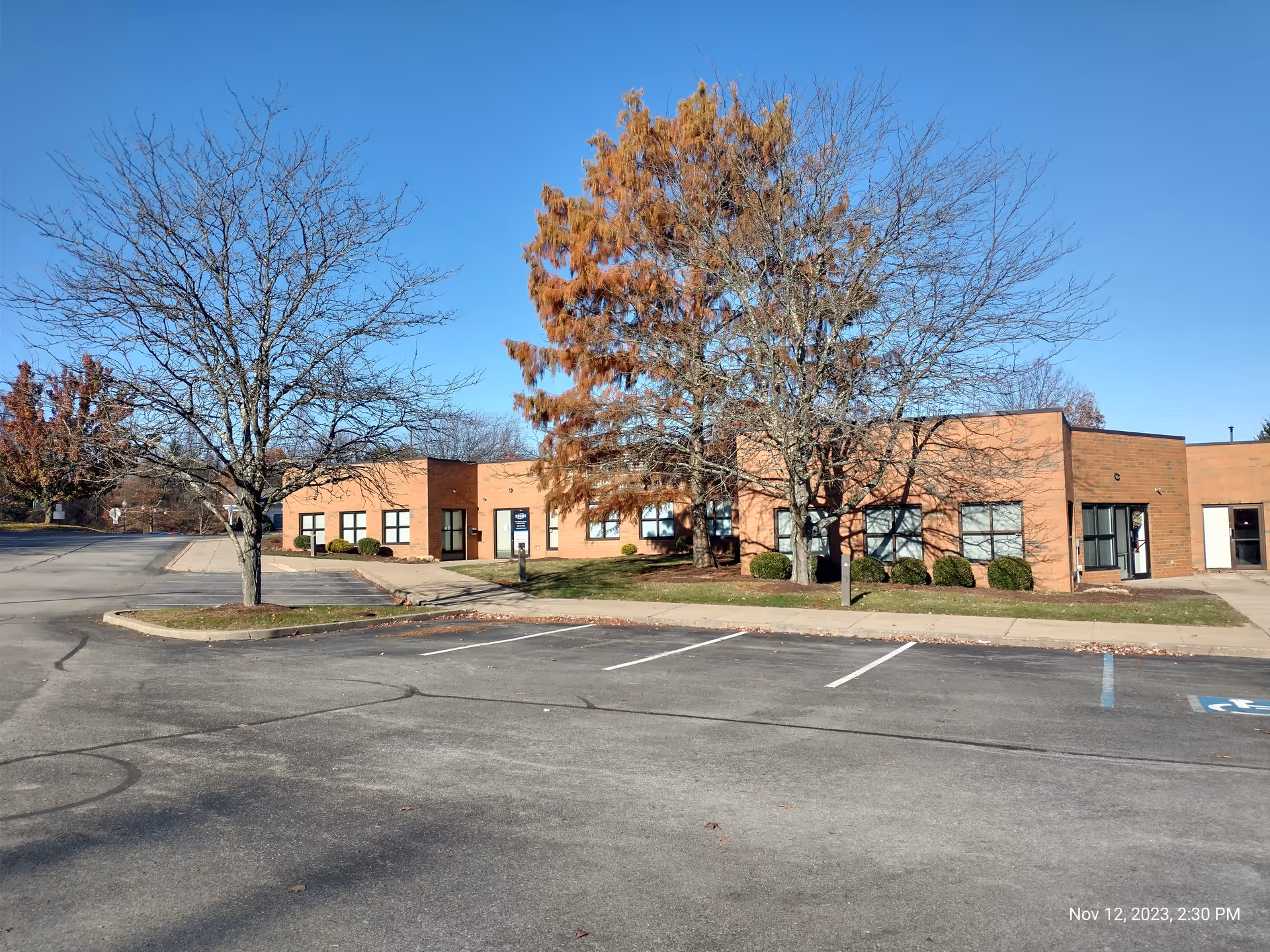 Brick exterior facility with parking lot and leafless trees under a clear blue sky.