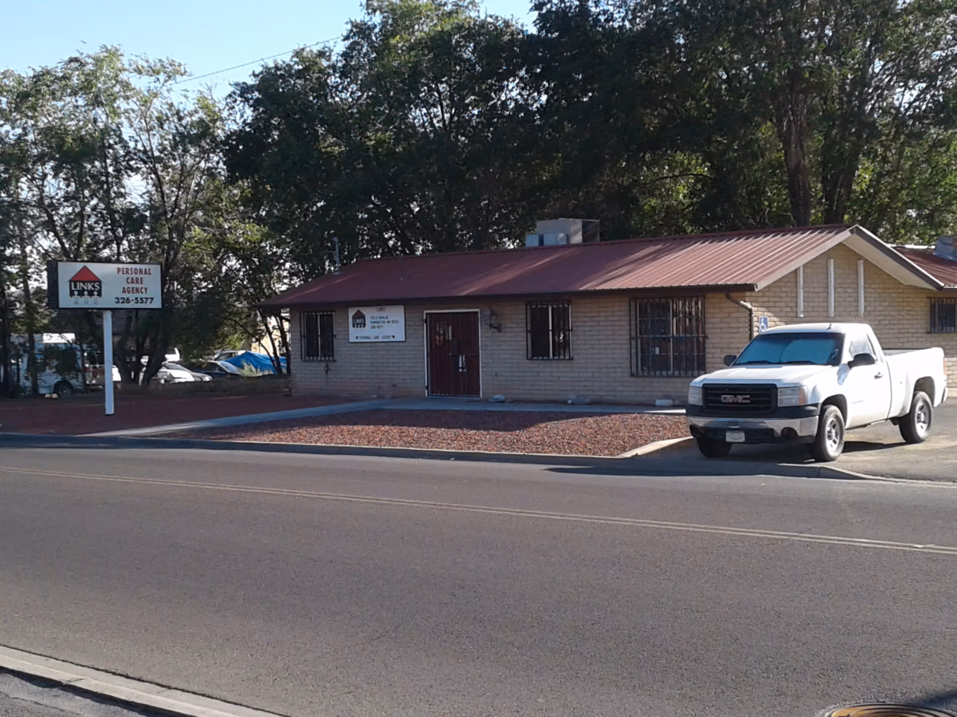 Exterior of a single-story brick building with a red roof and a white pickup in front.