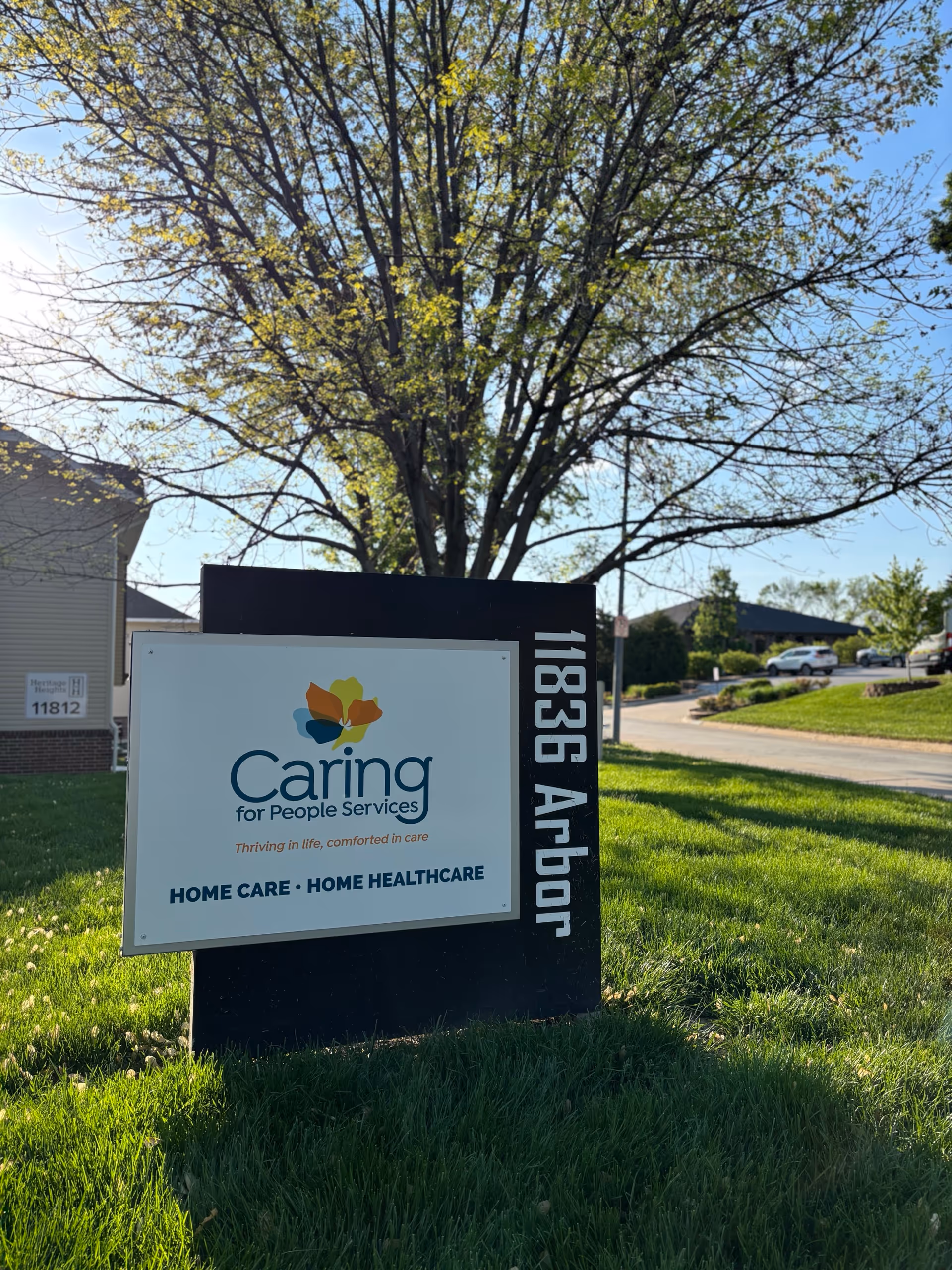 Outdoor sign for Caring for People Services in a grassy, tree-lined area.