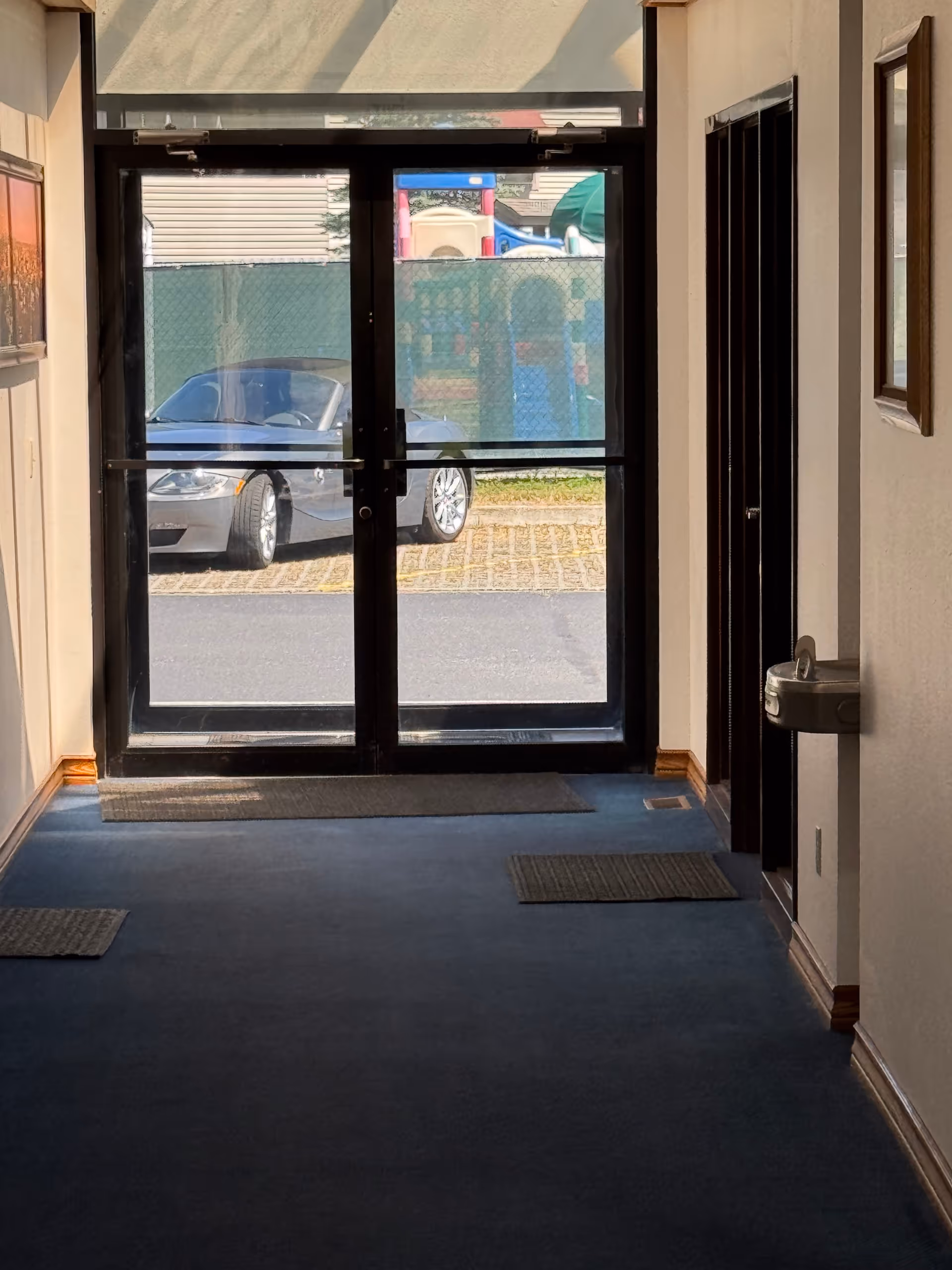 Sunlit interior hallway with glass double doors opening to a parking lot.