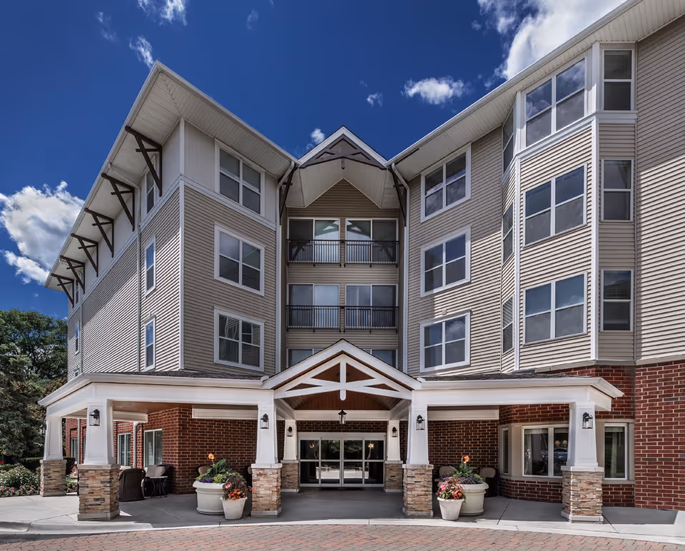 Three-story senior living building with brick base, beige siding, and a covered front entrance.