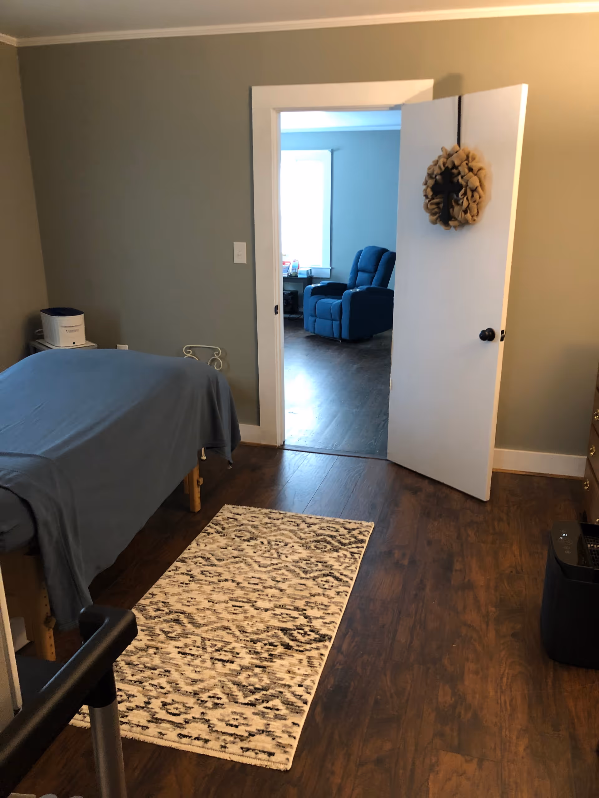 Bedroom in a senior living facility with a bed, rug, doorway to a living area beyond.