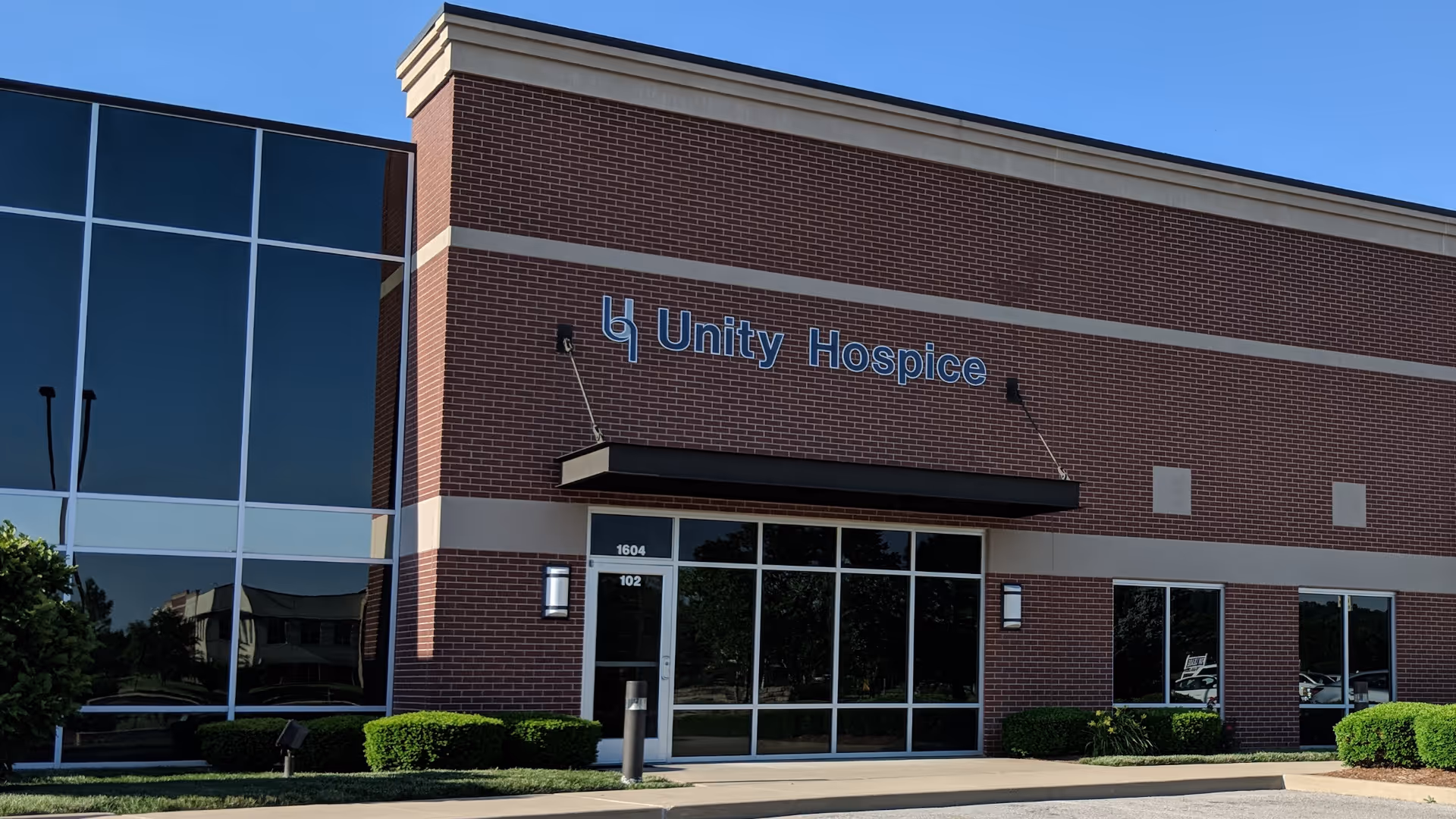 Exterior view of Unity Hospice building with glass entrance and blue sky.