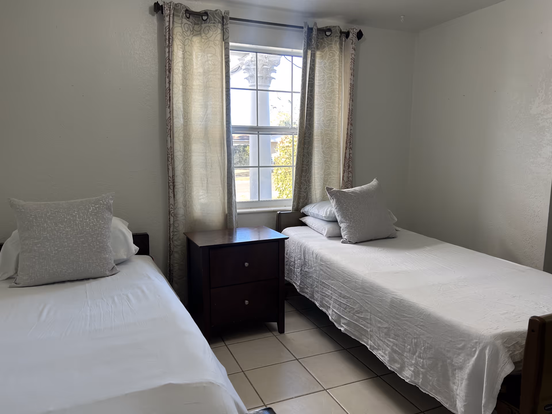 Two single beds with a nightstand between, near a window with curtains.