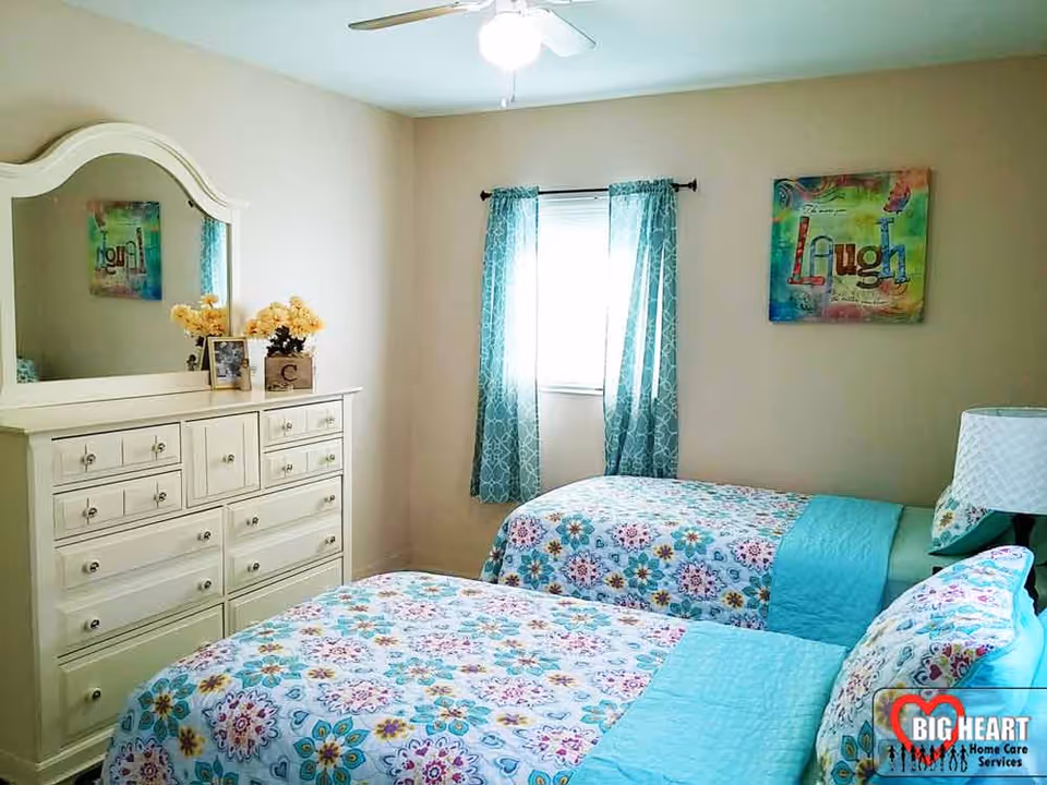 Two twin beds with floral turquoise bedding in a bright shared bedroom, dresser and wall art.