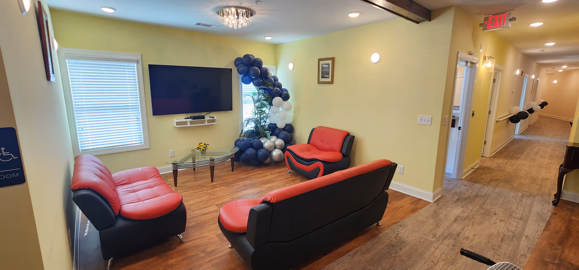 Lounge area in a senior living facility with red-and-black sofas and balloons.
