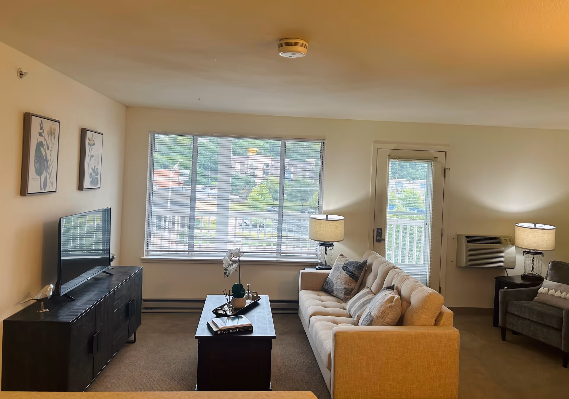 Sunlit living room featuring a beige sectional sofa, coffee table, TV, and large window views.