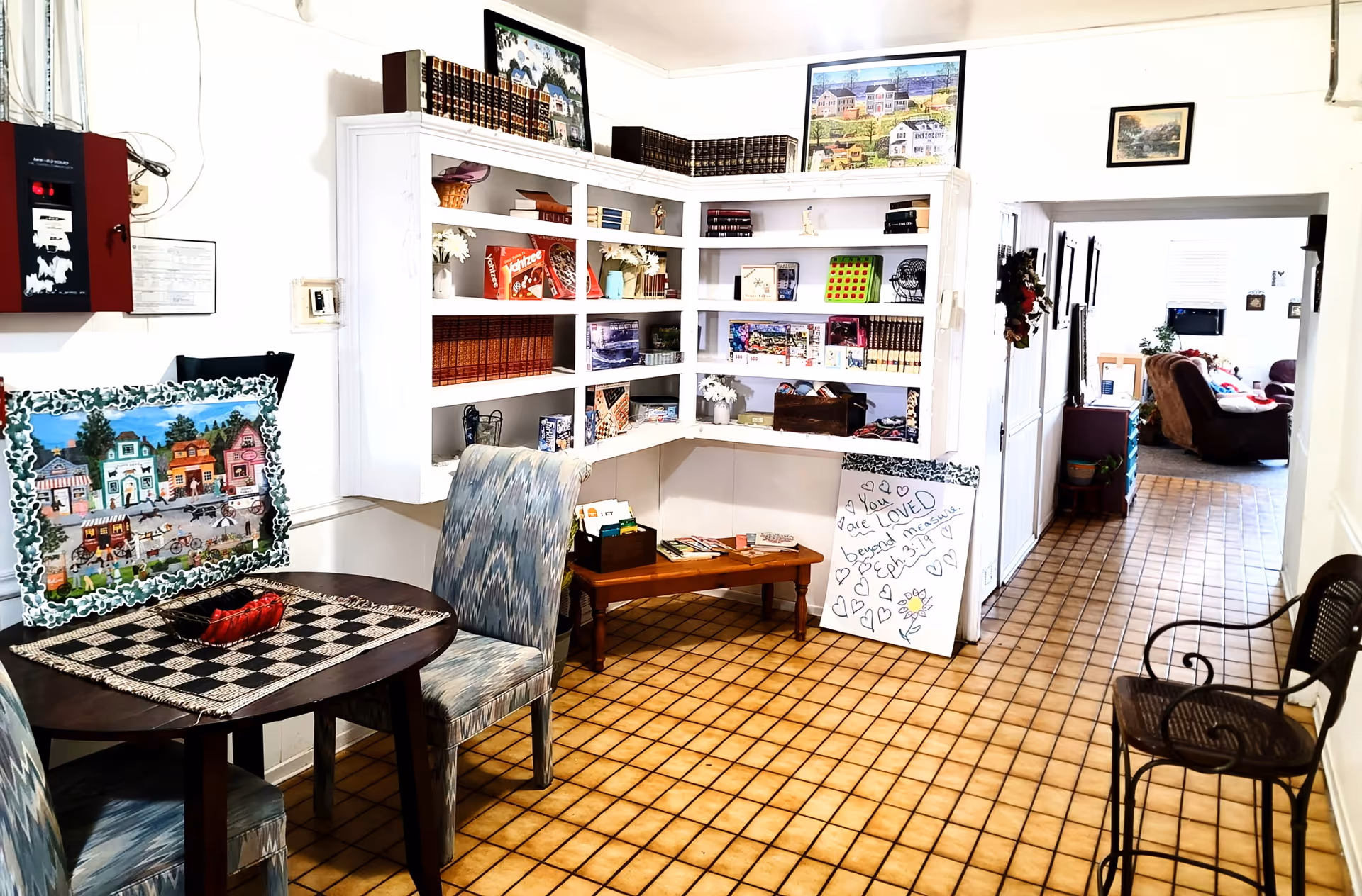 Indoor common area of Winters Assisted Living with white shelves, a round table, and tiled floor.