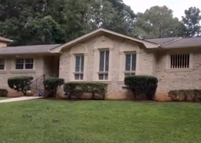 Exterior view of a single-story building with windows, bushes, and a green lawn.