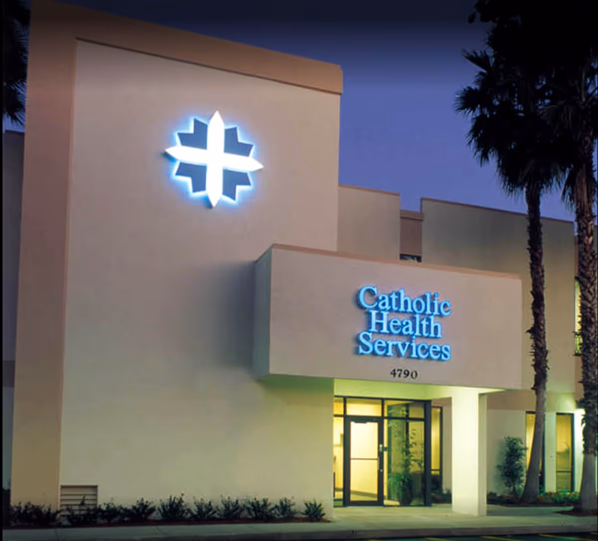 Exterior view of Catholic Health Services building at dusk with illuminated logo and entrance.