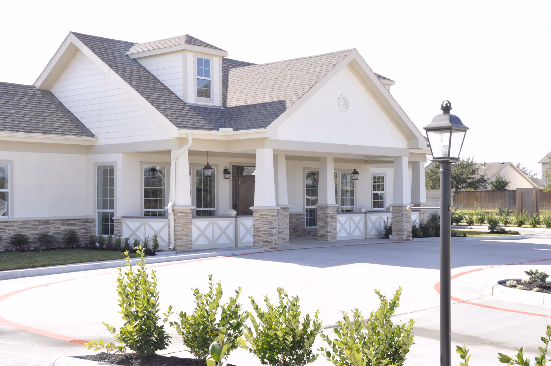 White senior living facility front with covered porch, stone accents, and manicured landscaping.