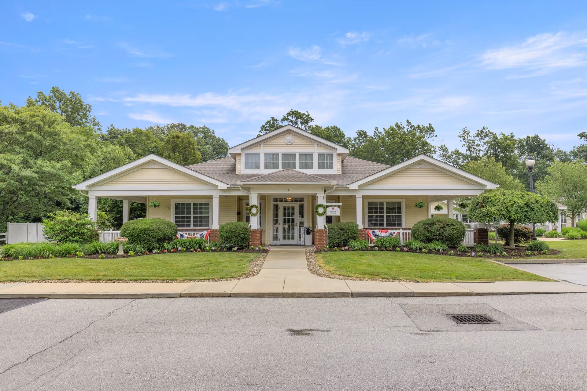 Single-story senior living facility front with beige siding, pillars, wreaths, and manicured landscaping.