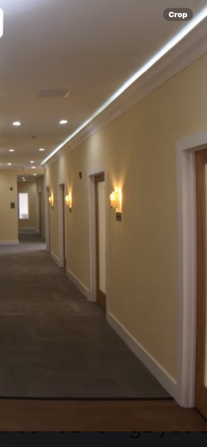 Long hallway in a senior living facility with doors, wall sconces, and carpet.