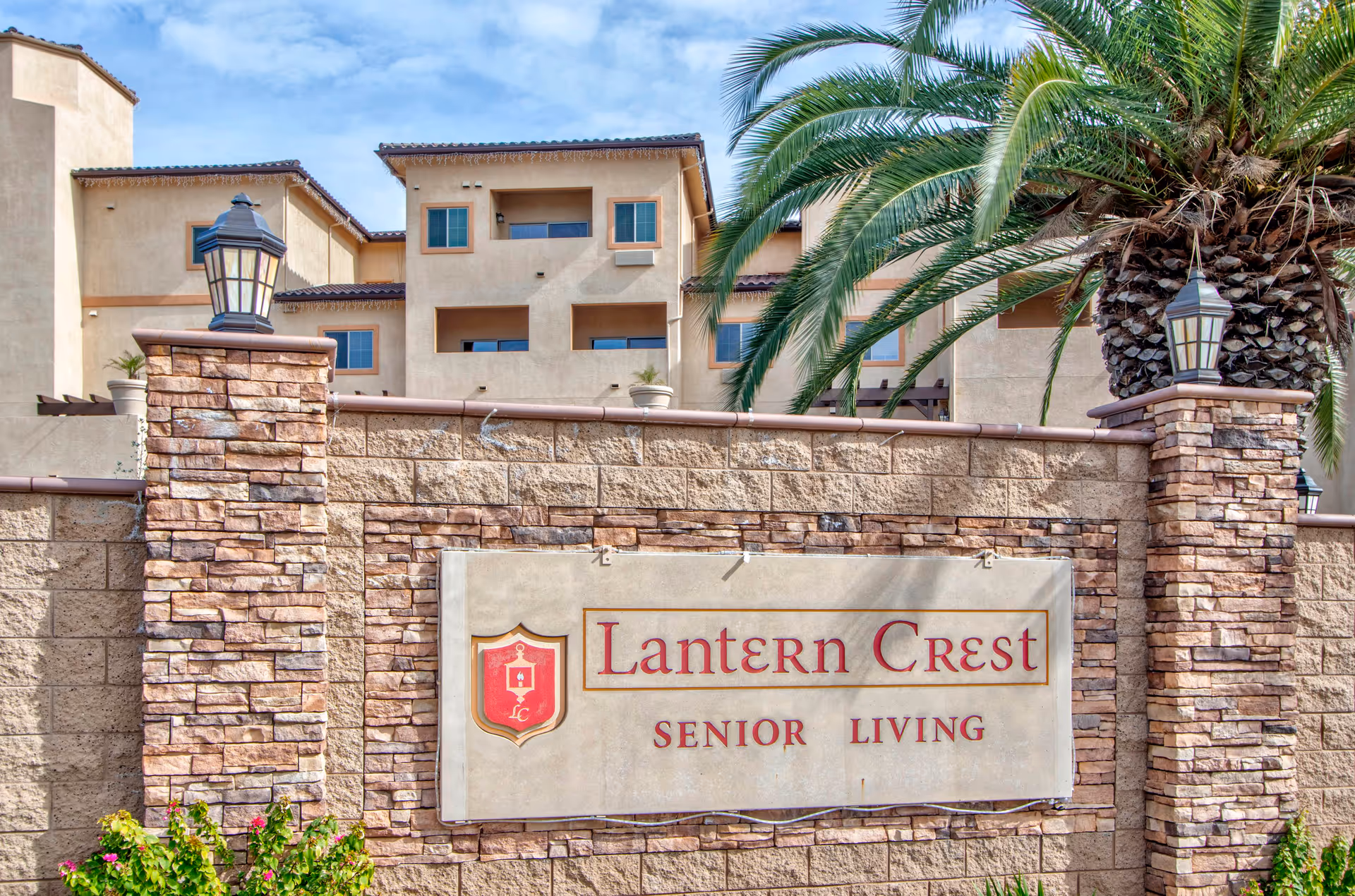 Front view of Lantern Crest Senior Living facility with stone sign and palm trees