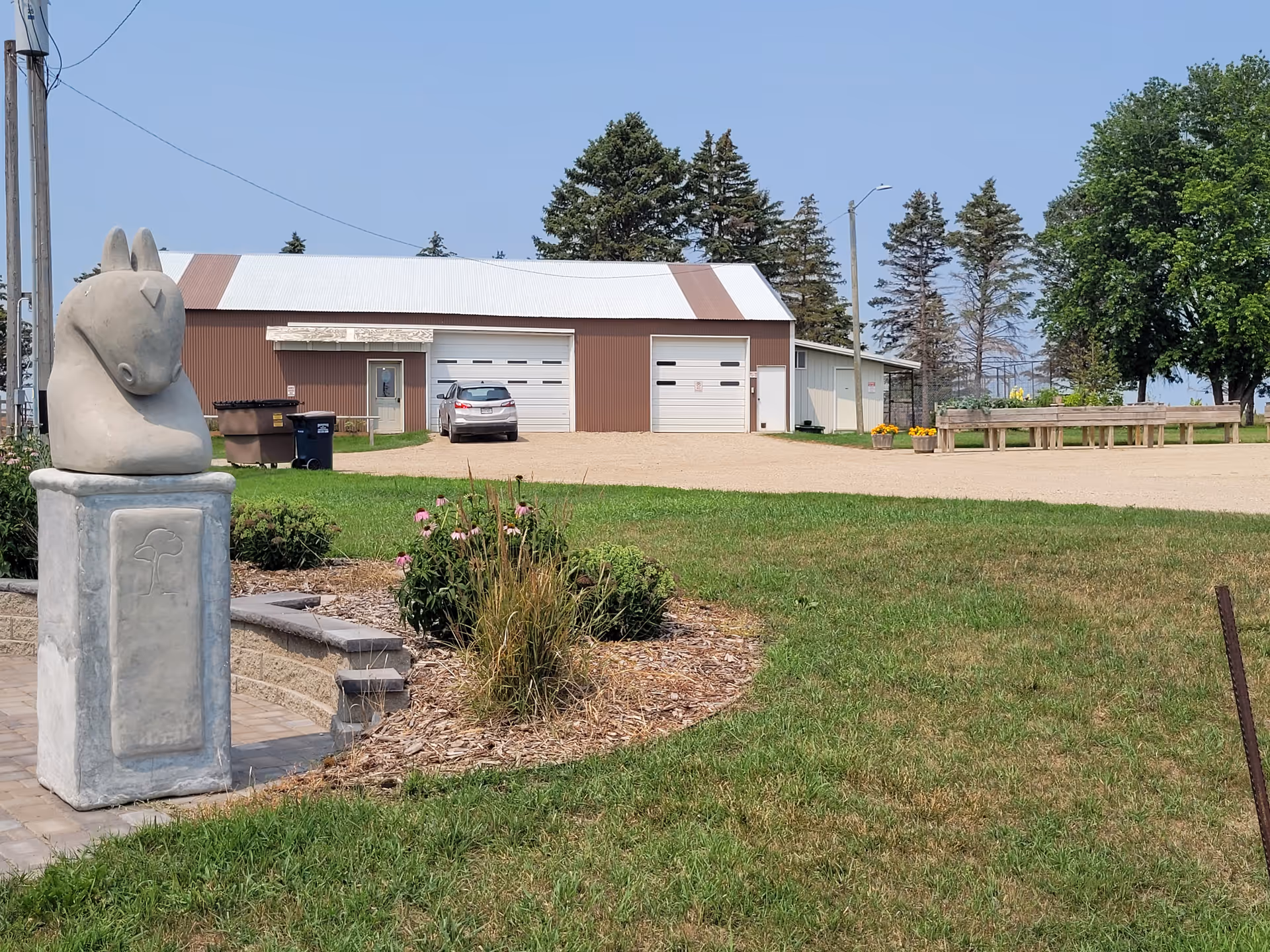 Outdoor view of a rural facility with a statue, brown-roofed building, and benches.