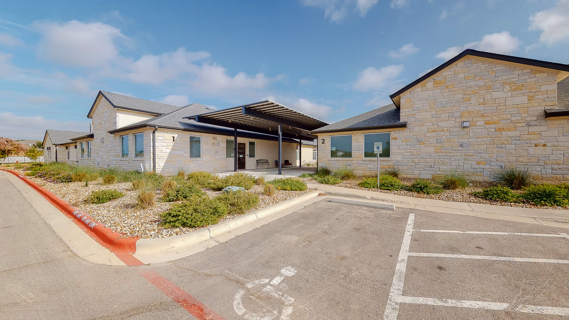 Stone-clad senior living facility exterior with entrance, parking spaces, and landscaped front beds.