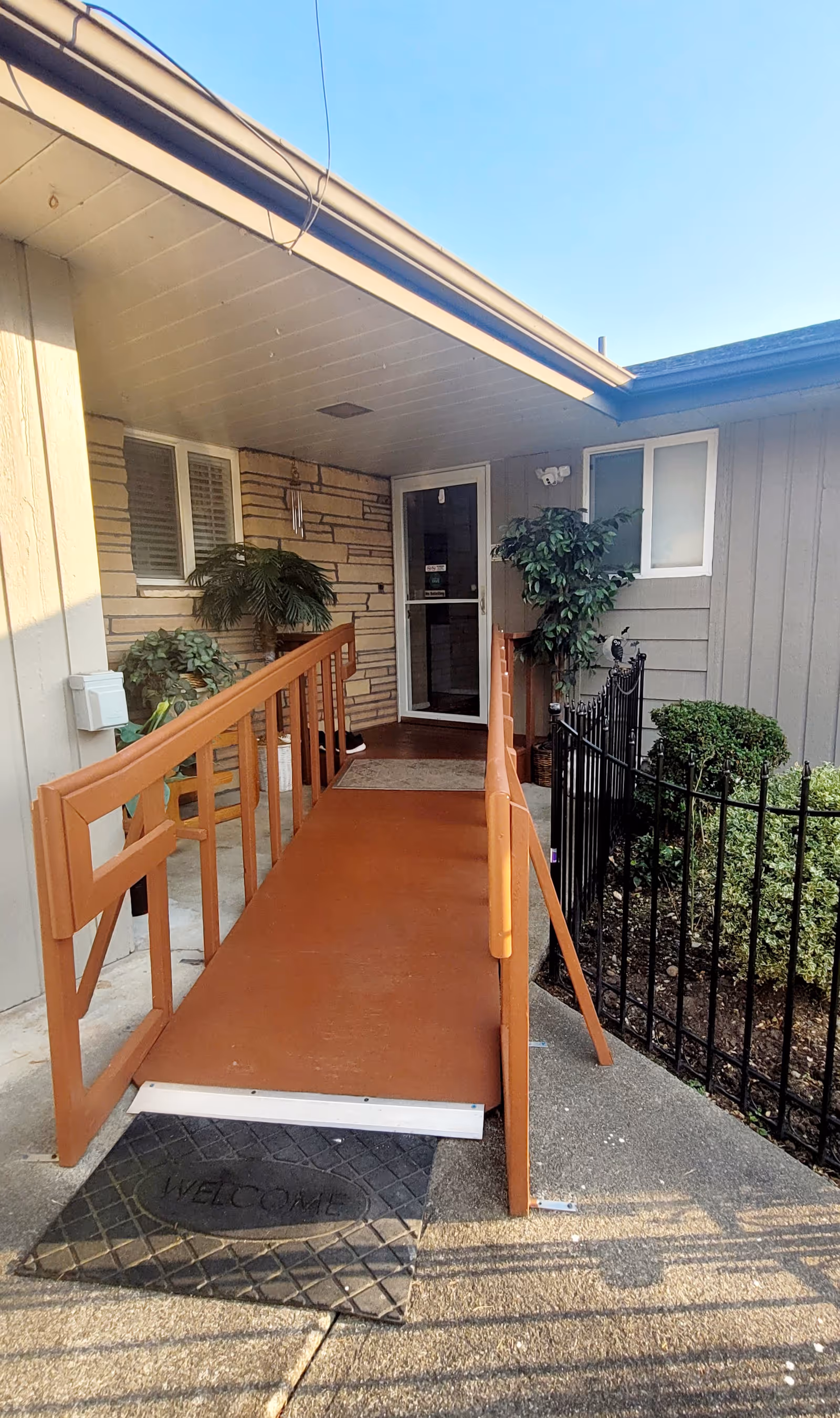 Front entrance of a senior living facility with a wooden ramp and a welcome mat.