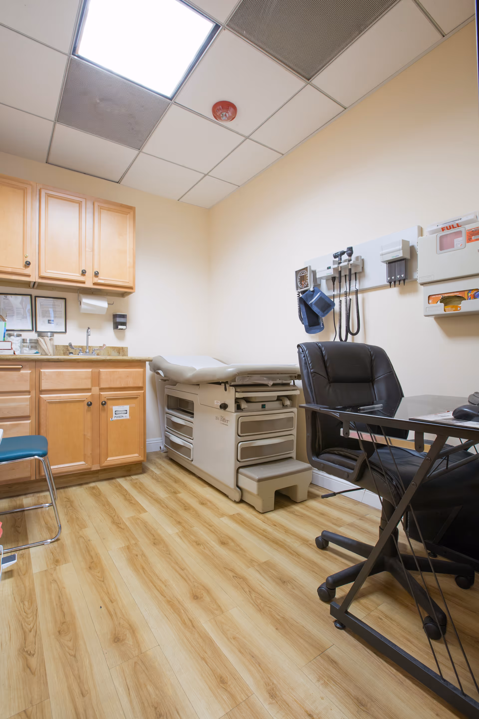 Medical examination room with a patient bed, medical equipment, cabinets, and a desk.
