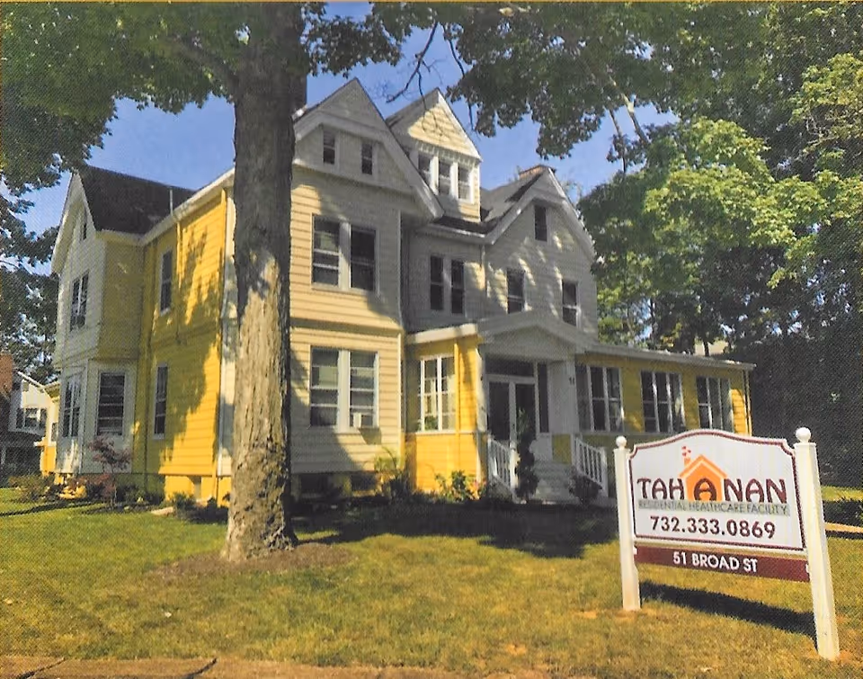 Exterior view of a yellow, multi-story senior living building with a sign in the front yard.