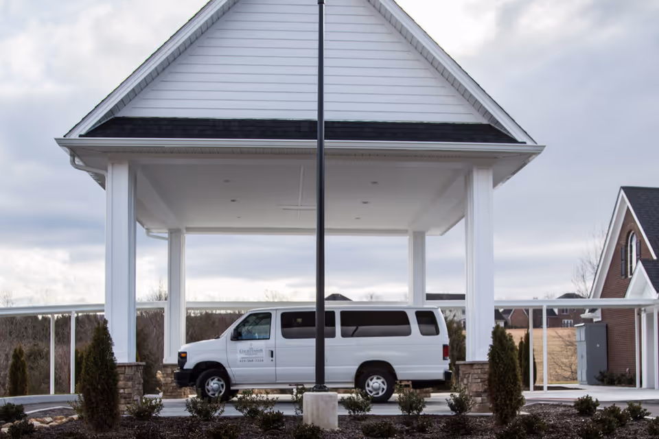 A white shuttle van parked under the covered entrance/porte-cochère of a senior living facility.
