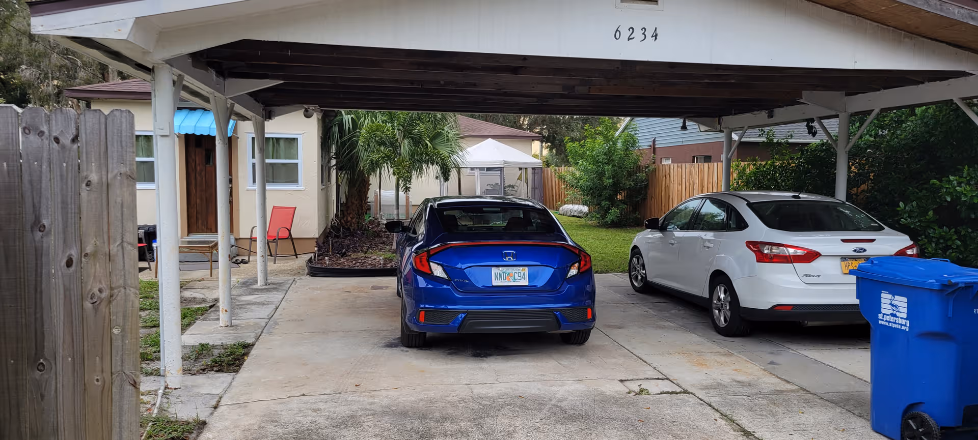Two cars parked under a covered carport in front of a residential building.